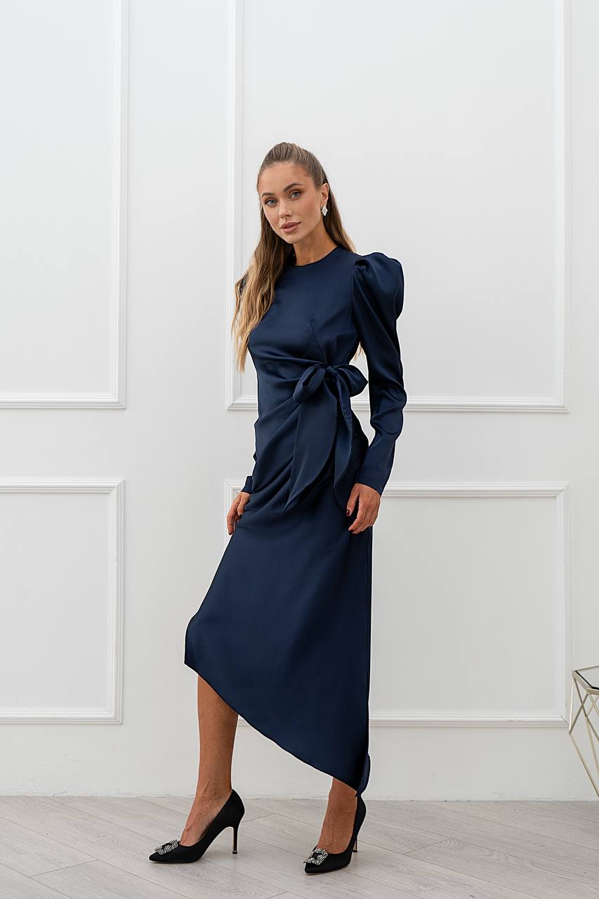 Woman wearing a navy blue dress with puff sleeves against a white paneled wall.