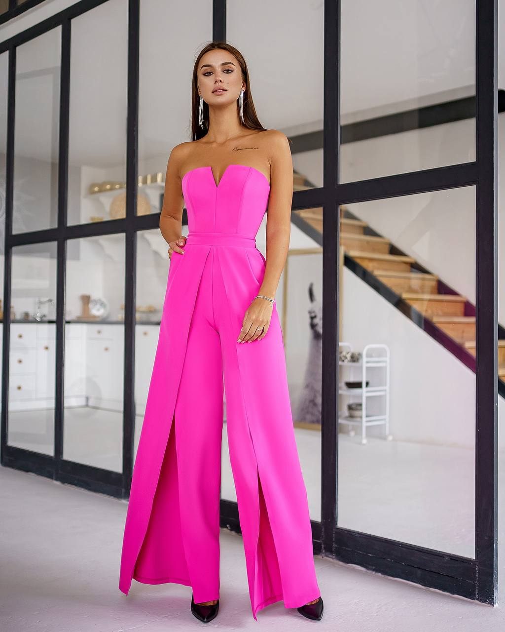 Woman wearing a bright pink strapless jumpsuit in an indoor setting.