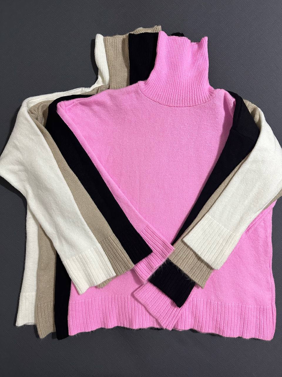 Pink turtleneck sweater with beige and black accents on a dark gray background