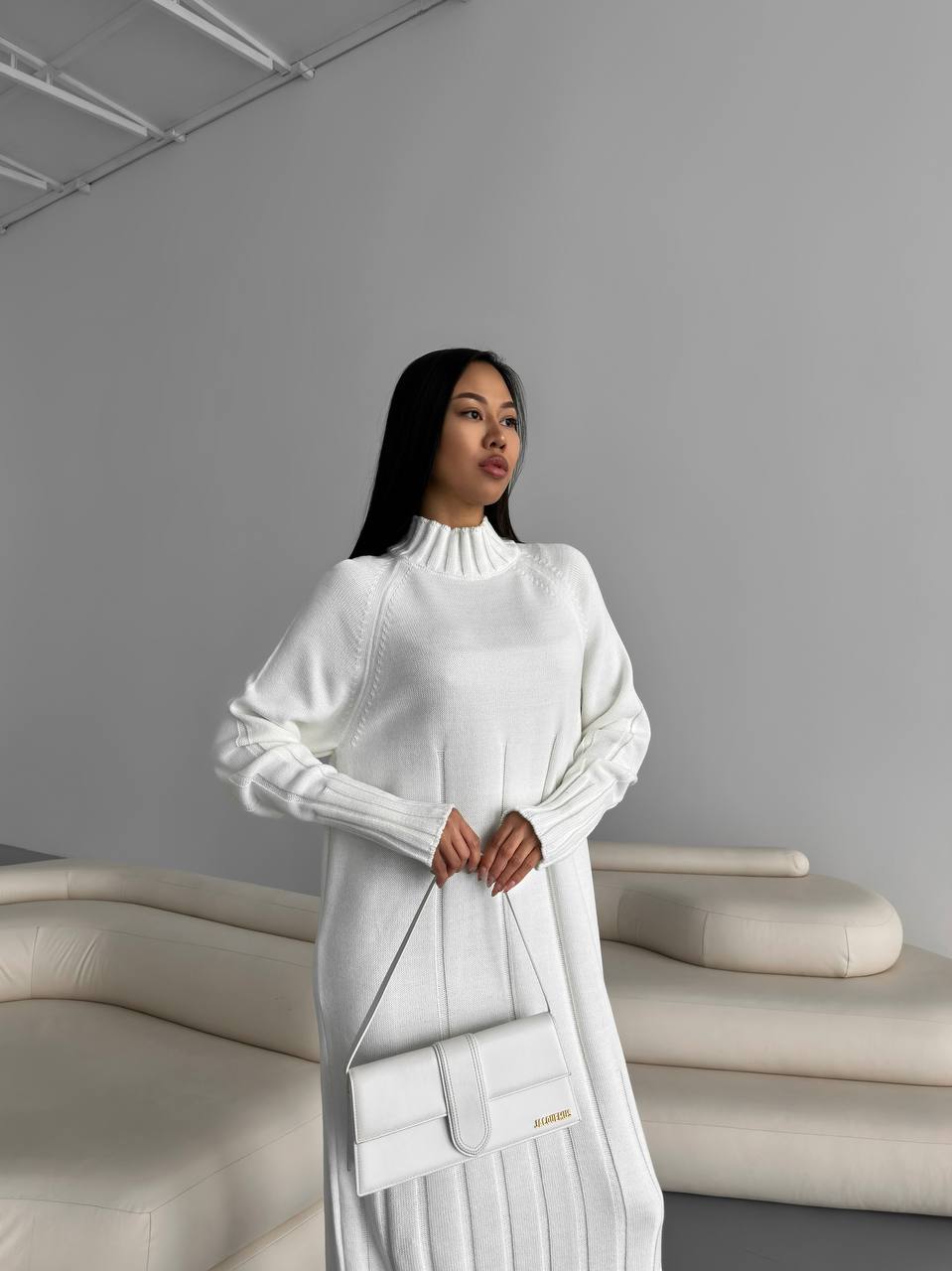 Woman in a white outfit holding a handbag in a minimalistic setting