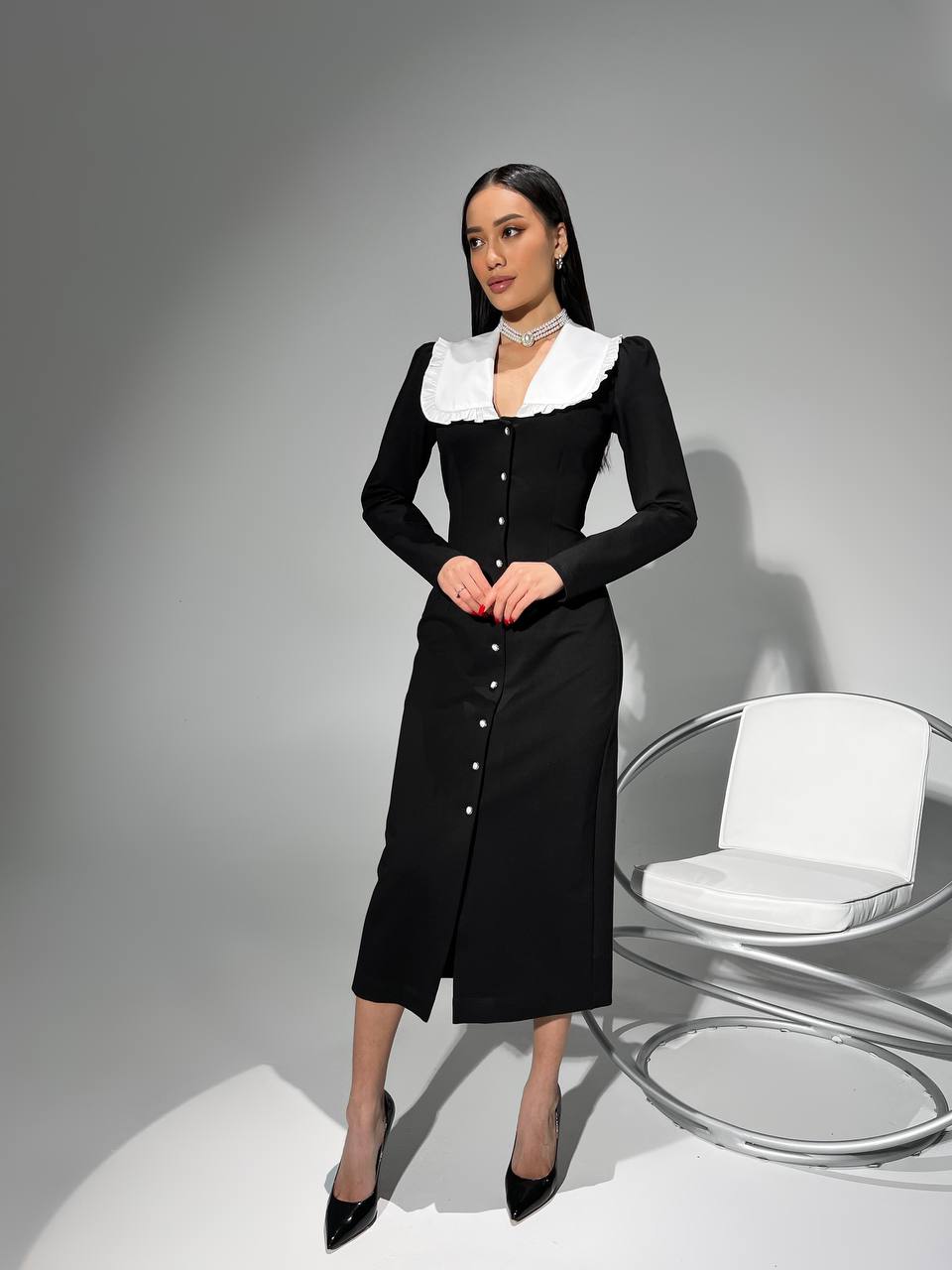 Woman wearing a black dress with white collar against a gray background