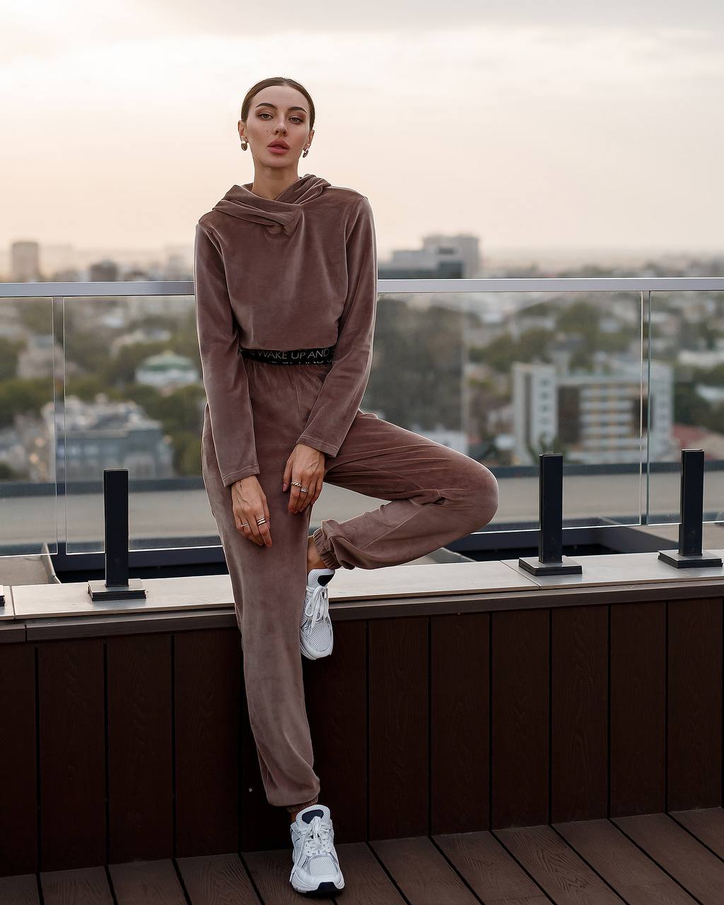 Woman in a brown tracksuit standing on a rooftop with cityscape in the background