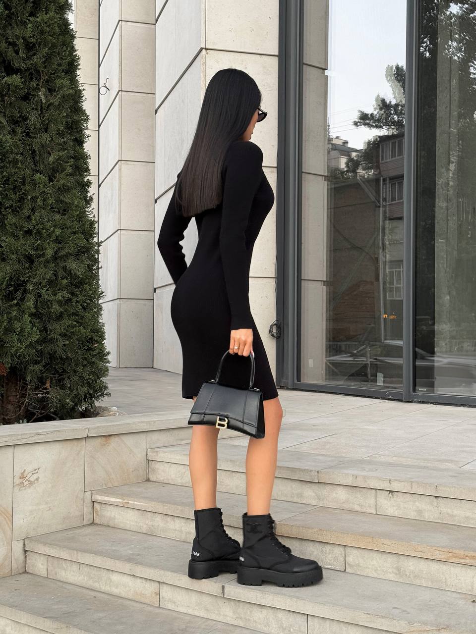 Woman in a black dress and boots standing on steps outside a building.