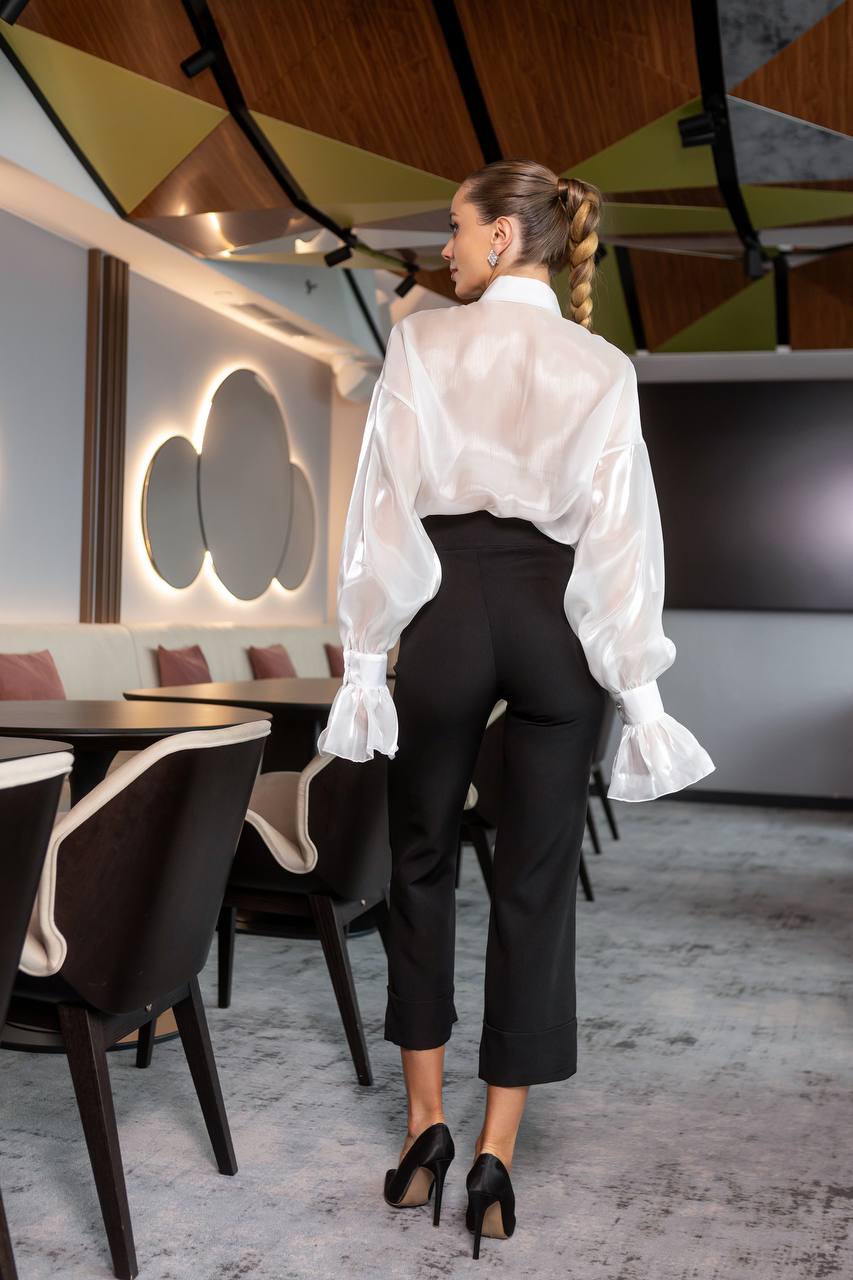 Woman in a white blouse and black pants standing in a modern restaurant.