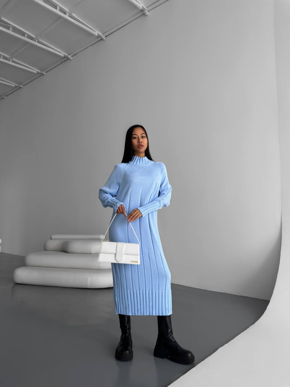 Woman in a light blue dress holding a white bag in a minimalistic setting