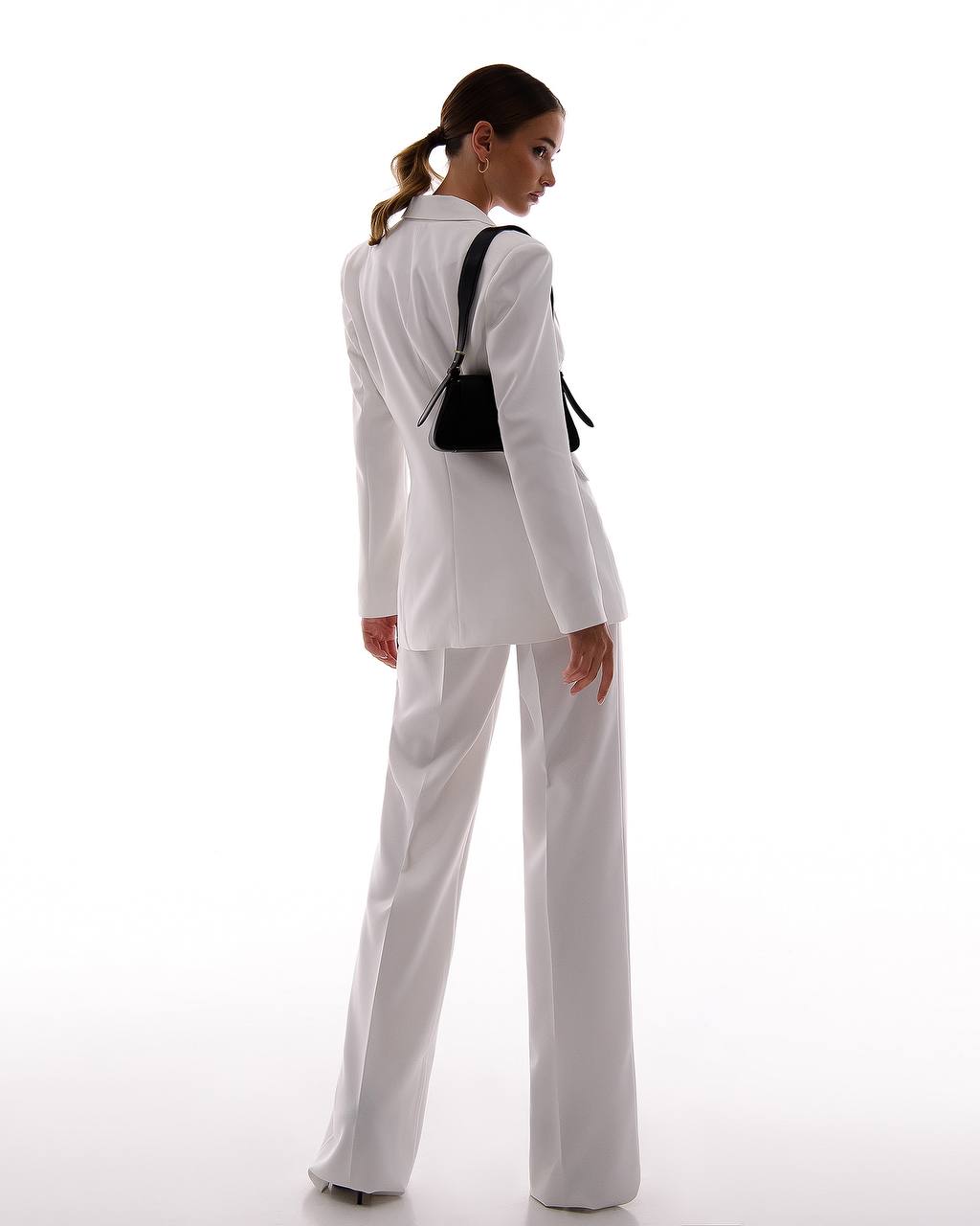 Woman wearing a white suit with a black handbag on a white background
