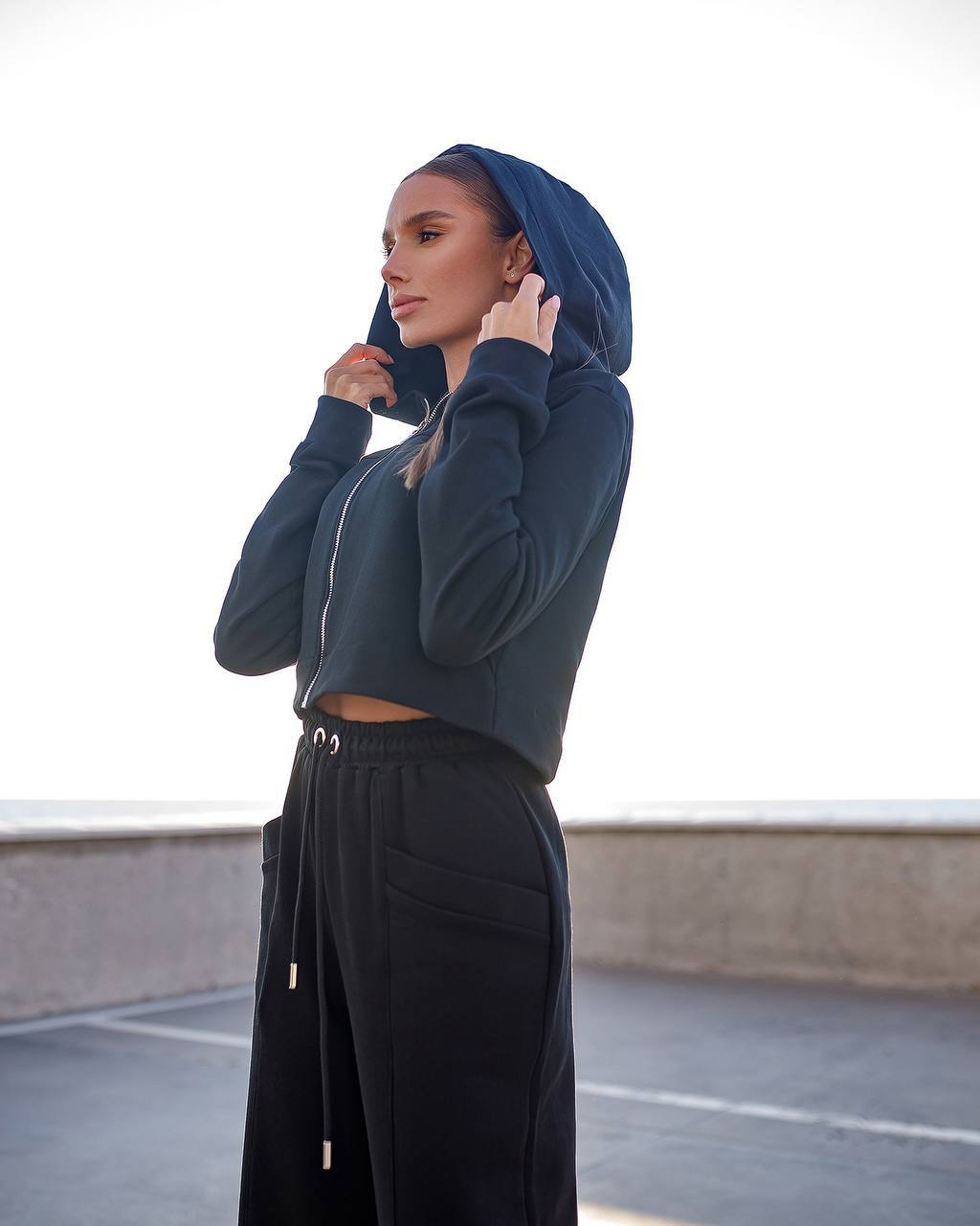 Person wearing a dark blue hoodie and black pants on a rooftop.