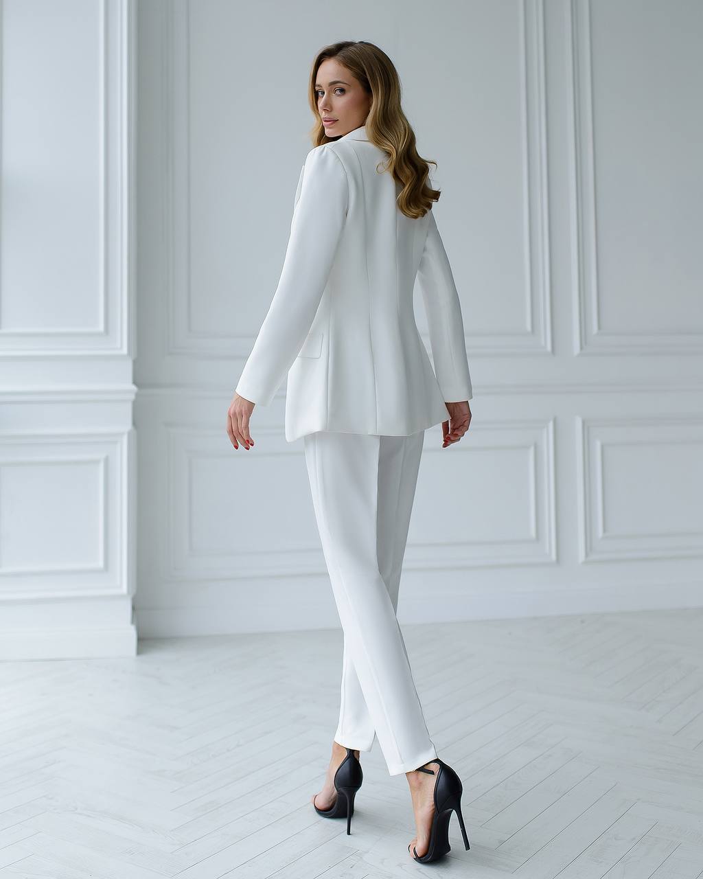 Woman wearing a white suit in a minimalistic room with white walls and floor.