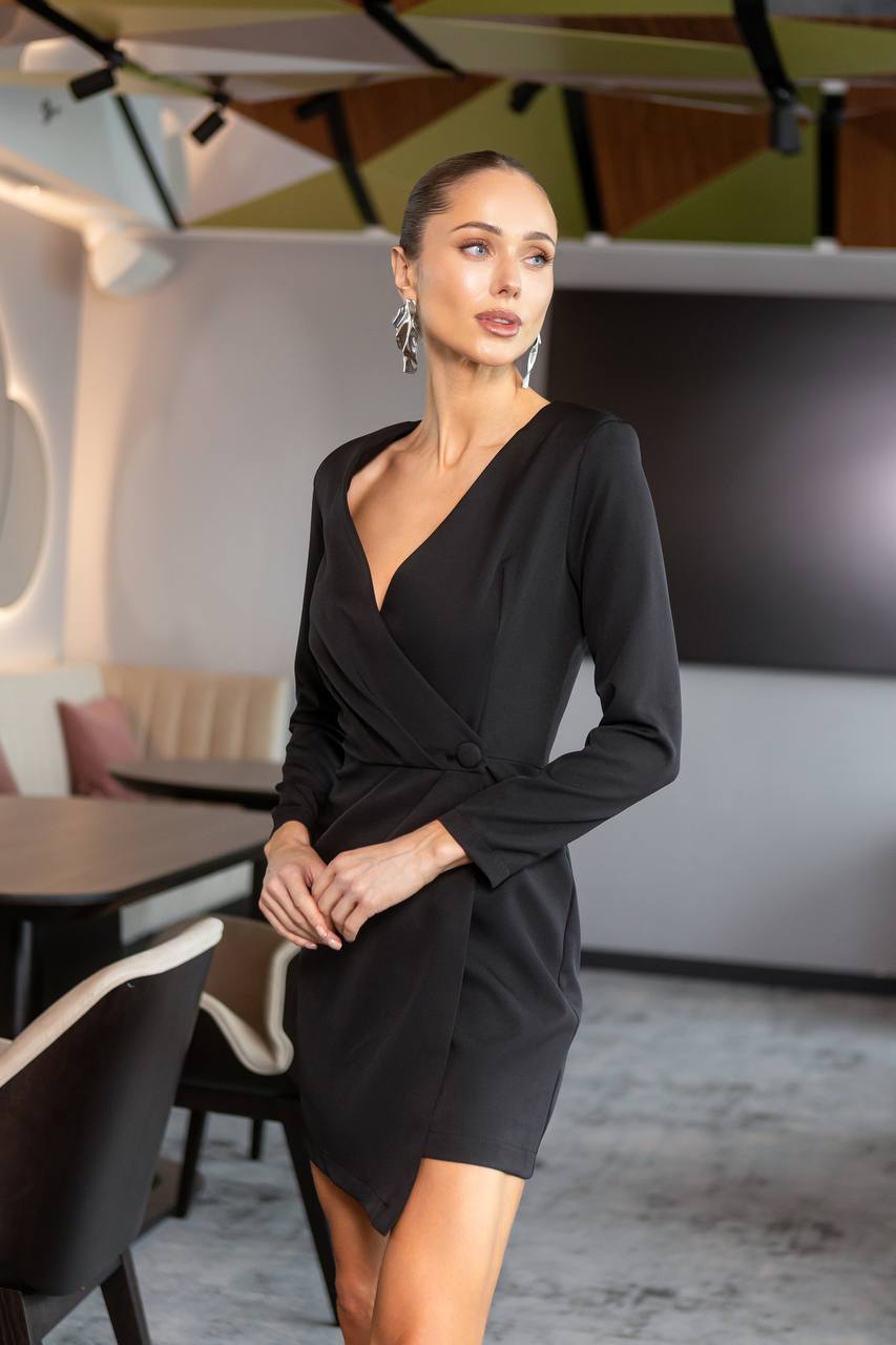 Woman in a black dress standing in an indoor setting with geometric wall art.