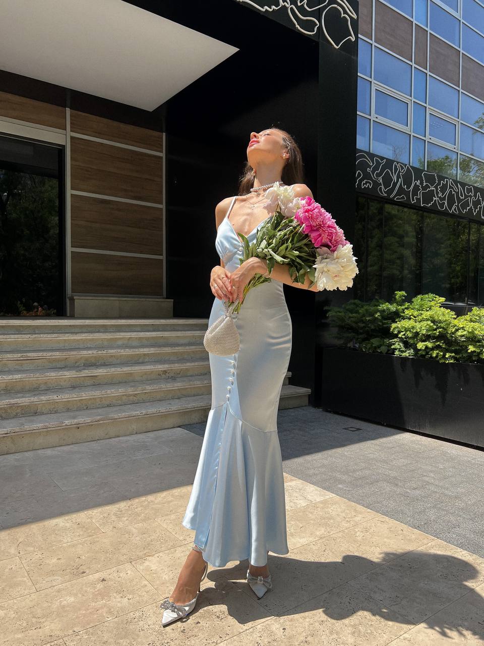 Woman in a light blue dress holding flowers in front of a building.