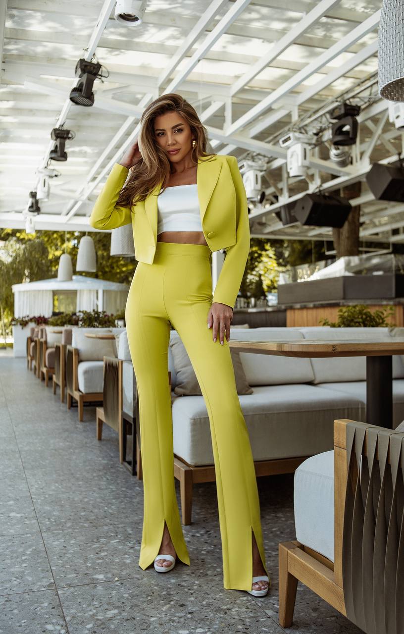Woman in a bright yellow suit standing in an outdoor setting with tables and chairs.