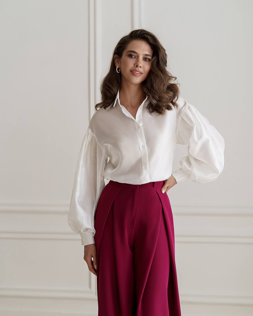 Woman wearing a white blouse and red pants against a light-colored wall