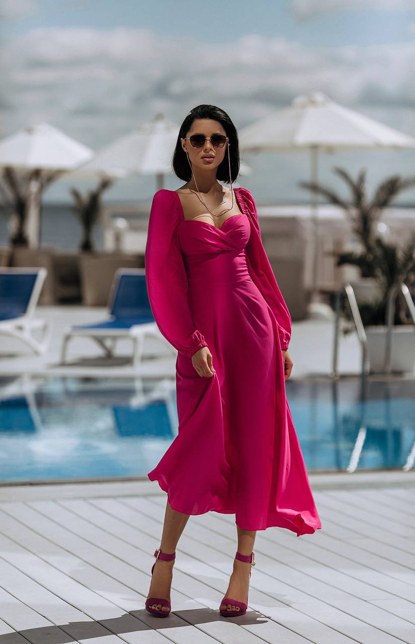 Woman in a pink dress standing by a poolside with a blurred background