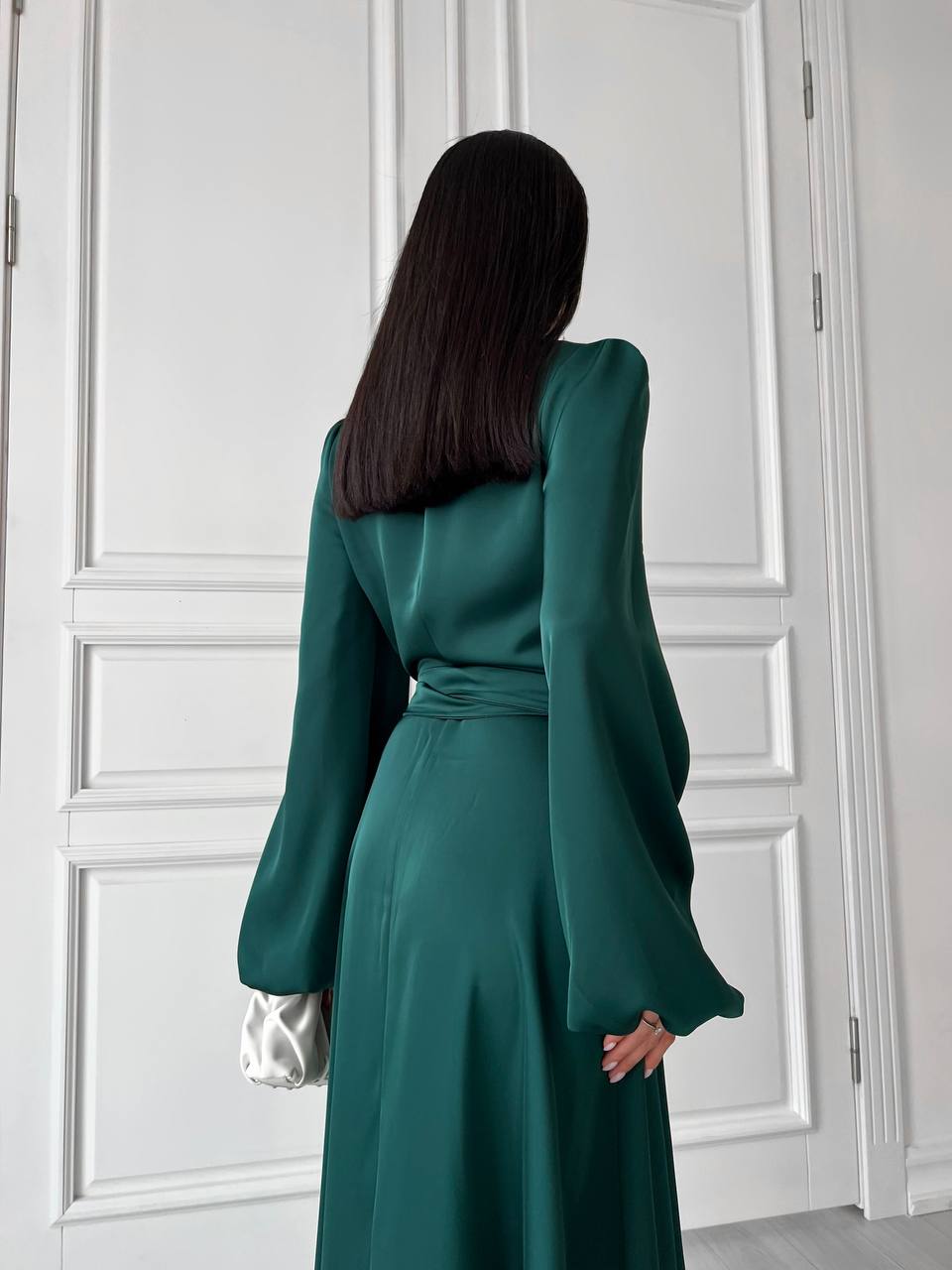 Woman wearing a green dress standing in front of a white paneled wall.