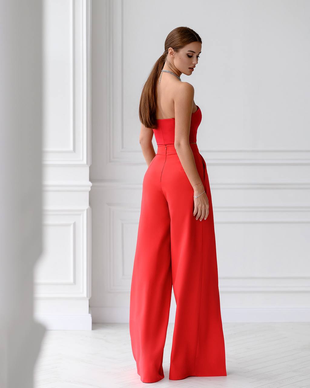 Woman wearing a red strapless jumpsuit in a white room
