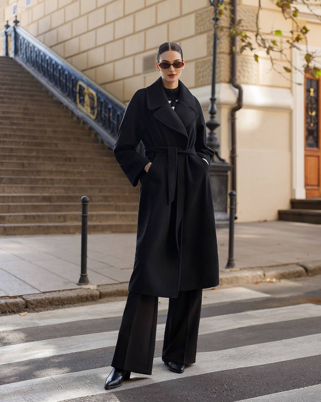 Person wearing a black coat and wide-leg pants on a city street.