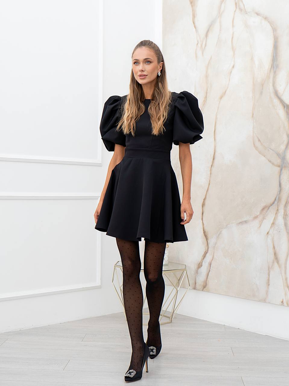 Woman wearing a black dress with puffed sleeves in a room with marble wall.