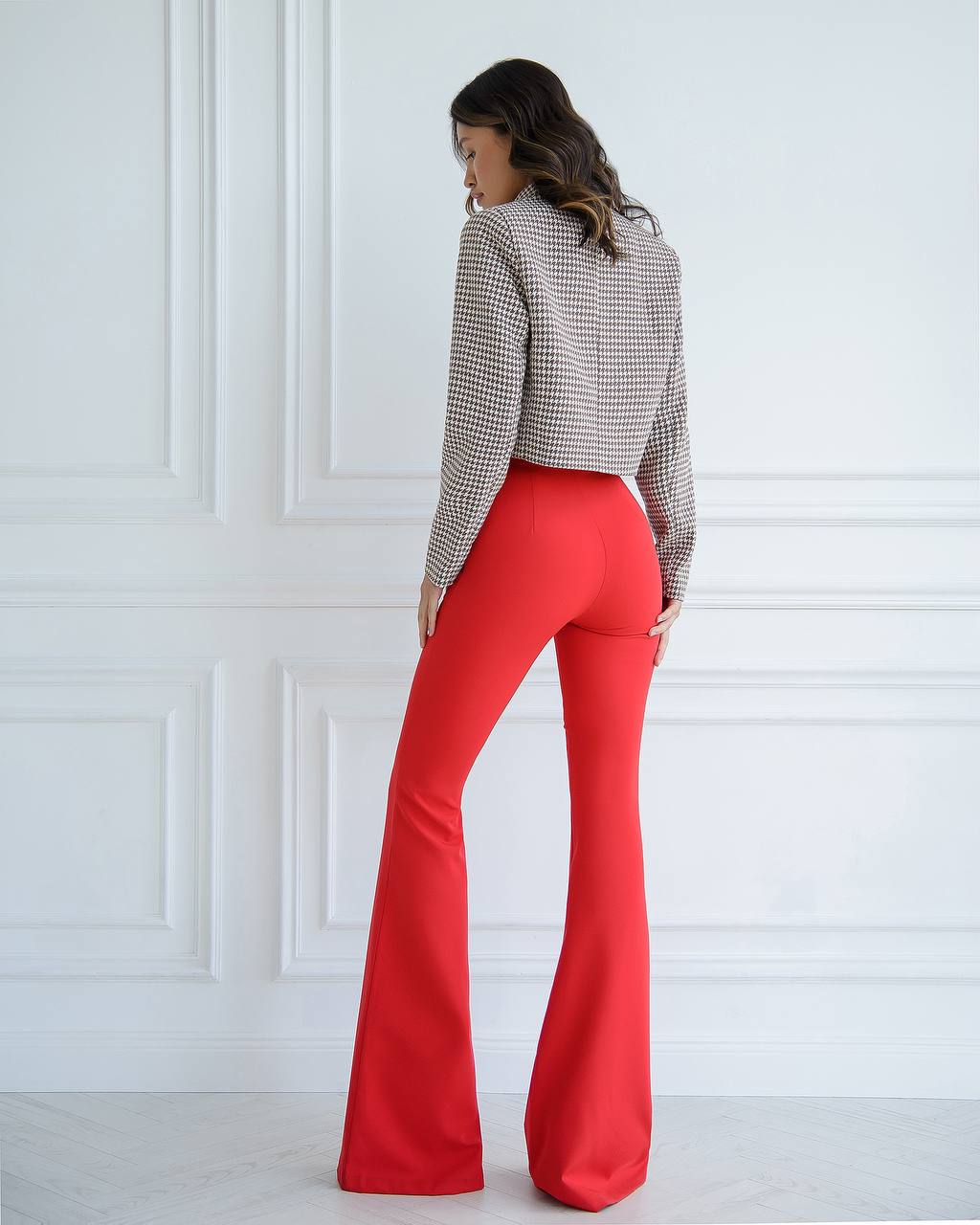 Person wearing red flared pants and a checkered shirt against a white wall
