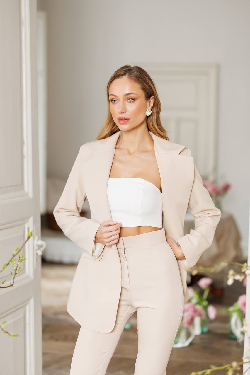 Woman wearing a beige suit with a white top in an indoor setting.