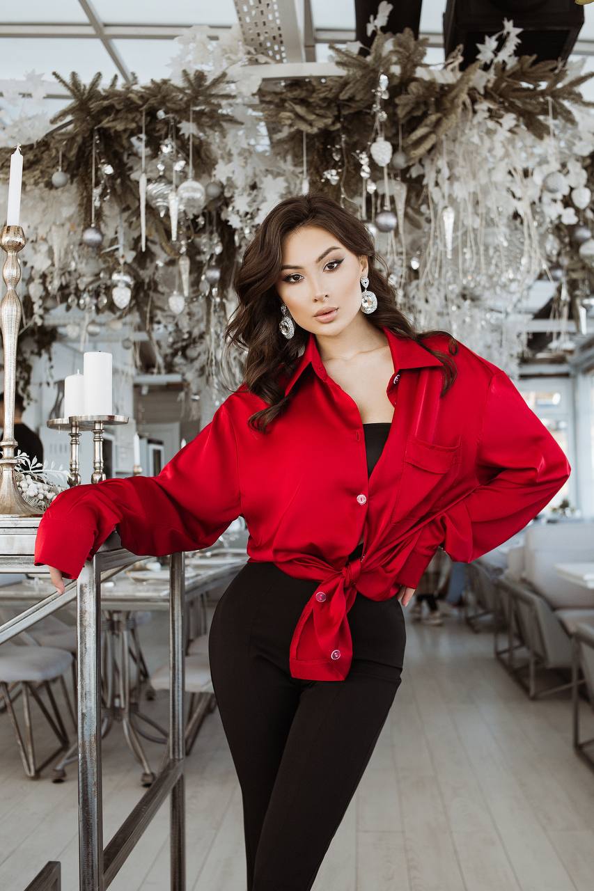 Woman in a red jacket standing in an elegant interior setting with decorative elements.