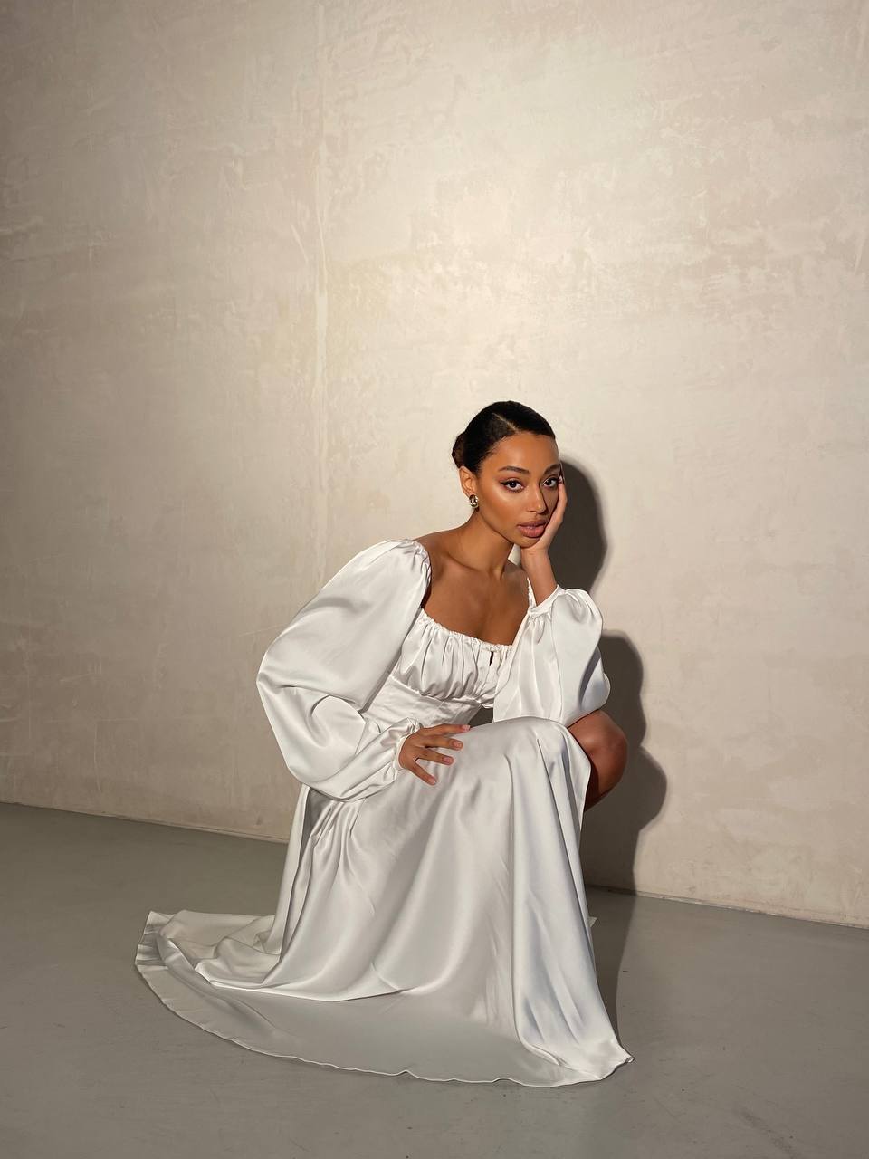 Woman in a white dress sitting against a plain background