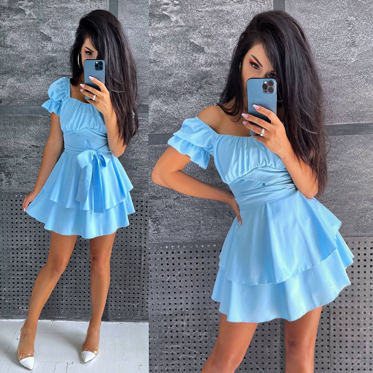 Woman wearing a light blue dress taking a mirror selfie against a gray textured wall.