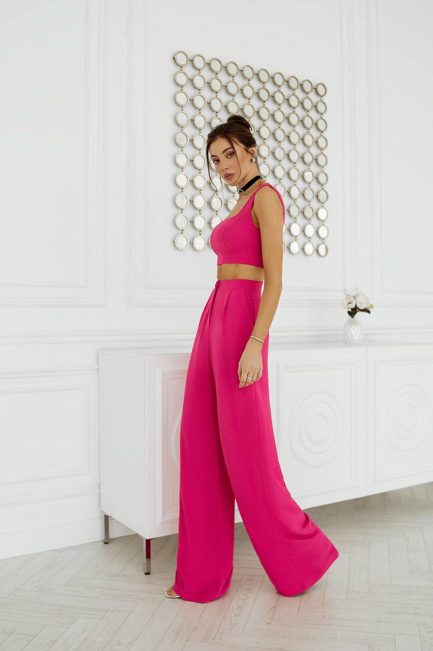 Woman in a bright pink outfit standing in a room with white walls and decorative elements.