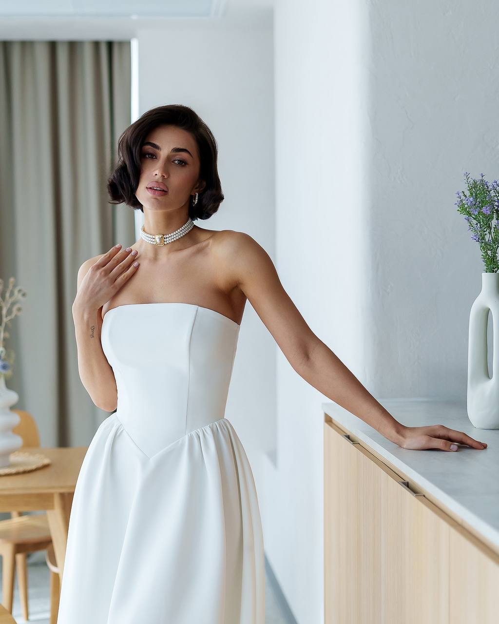 Woman in a strapless white dress standing in a modern kitchen.