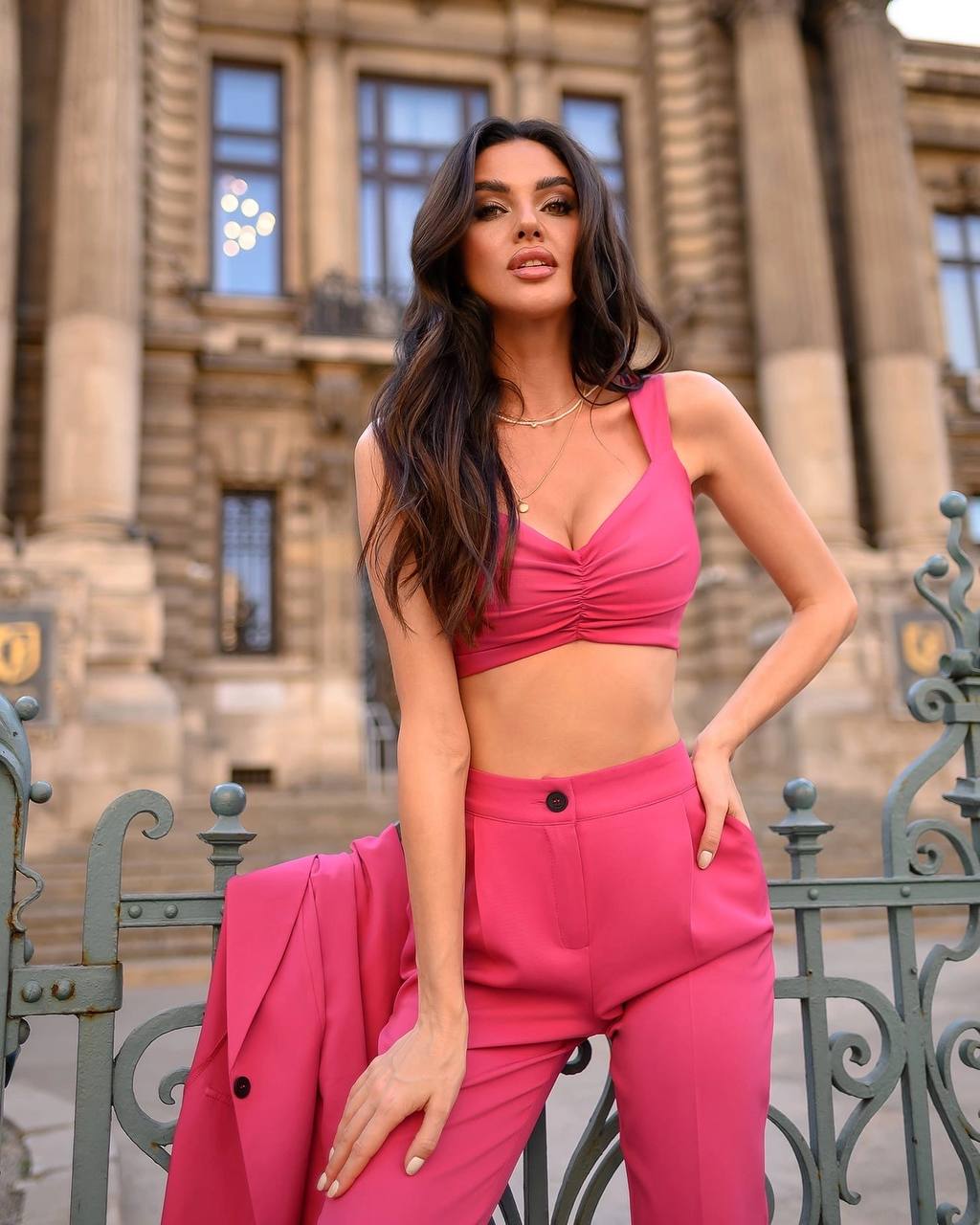 Woman in a pink outfit standing in front of a classical building