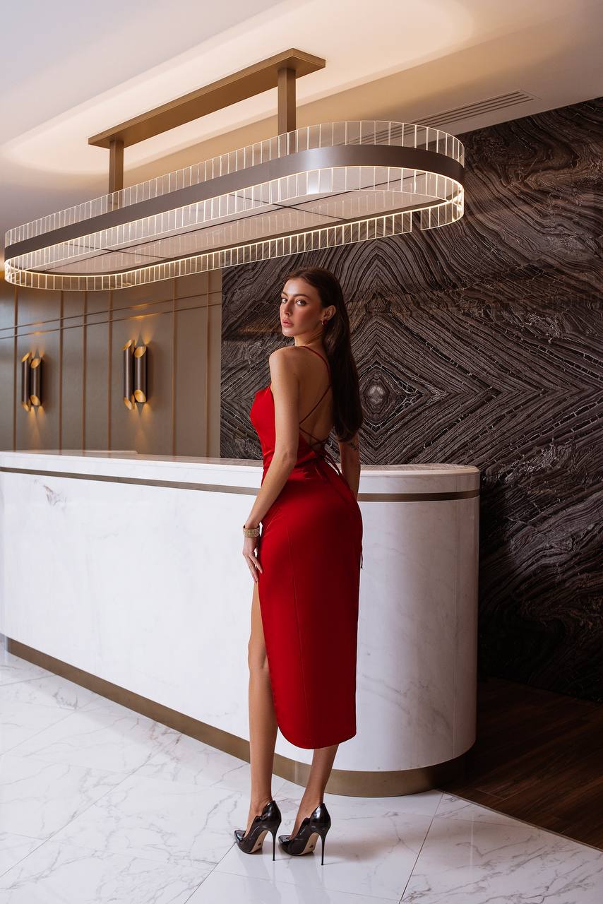 Woman in a red dress standing in a modern interior setting with a chandelier.