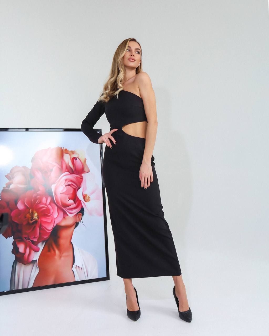 Woman in a black dress standing next to a screen displaying floral imagery on a white background