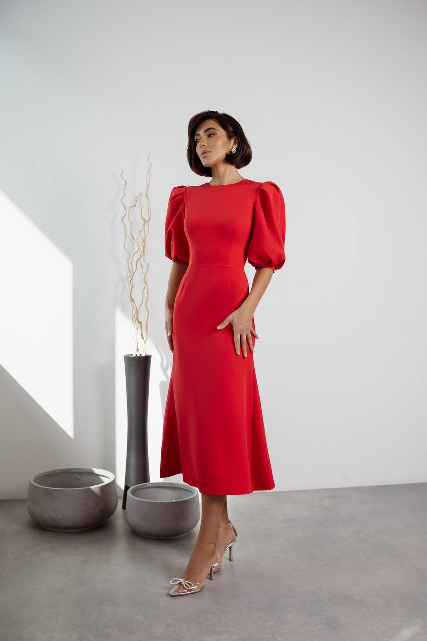 Woman in a red dress standing in a minimalistic room with white walls and gray floor.