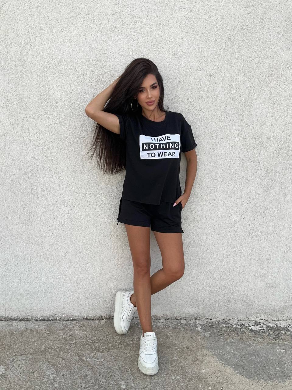 Woman wearing a black t-shirt with text and black shorts against a gray wall.