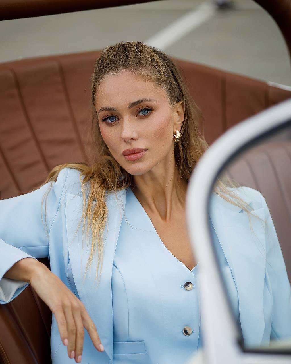 Woman in a light blue outfit sitting in a car with a brown interior.