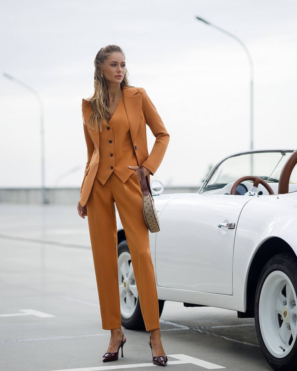Woman in a brown suit standing next to a white car