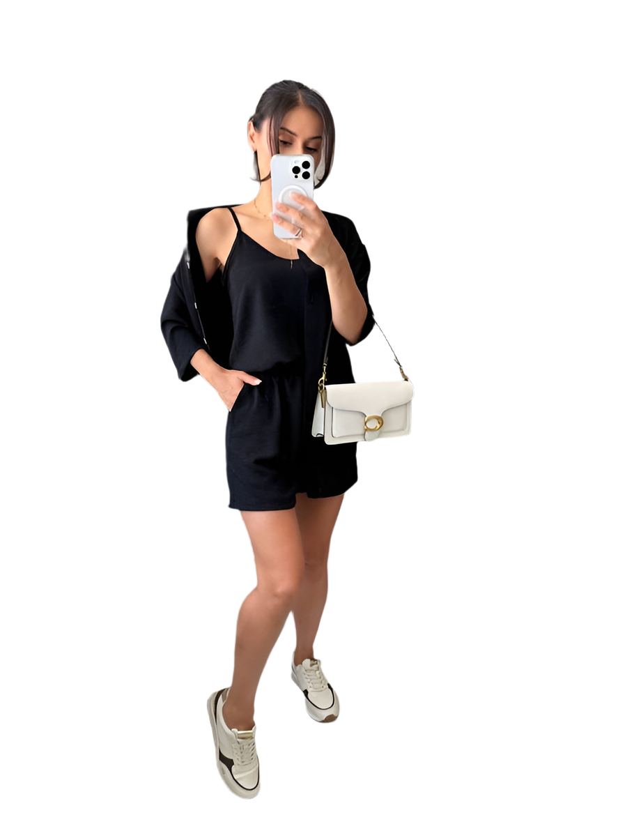 Woman taking a mirror selfie wearing a black outfit with a white handbag on a white background