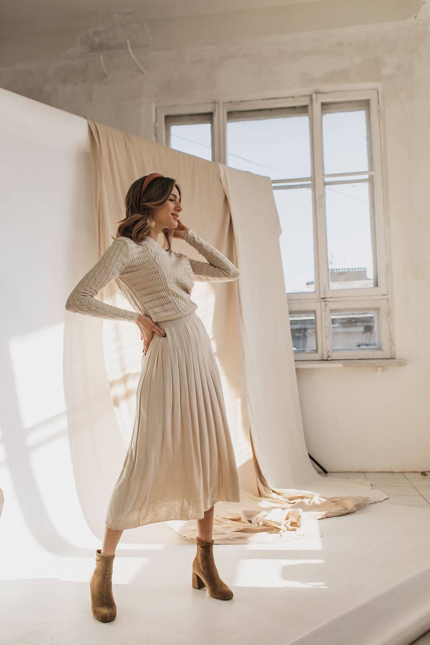 Woman in a long-sleeve dress standing in a room with large windows and white walls.