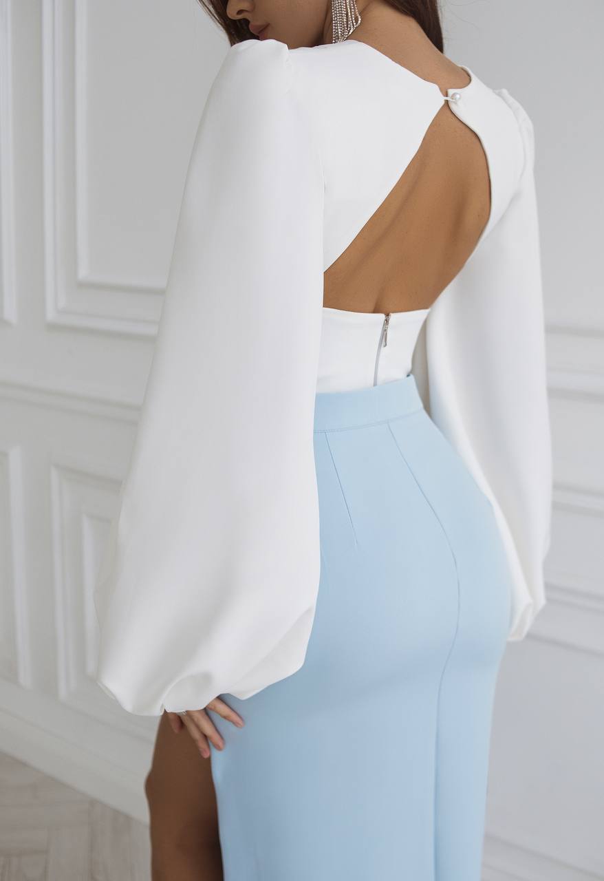 White open-back top and light blue pants against a white wall.