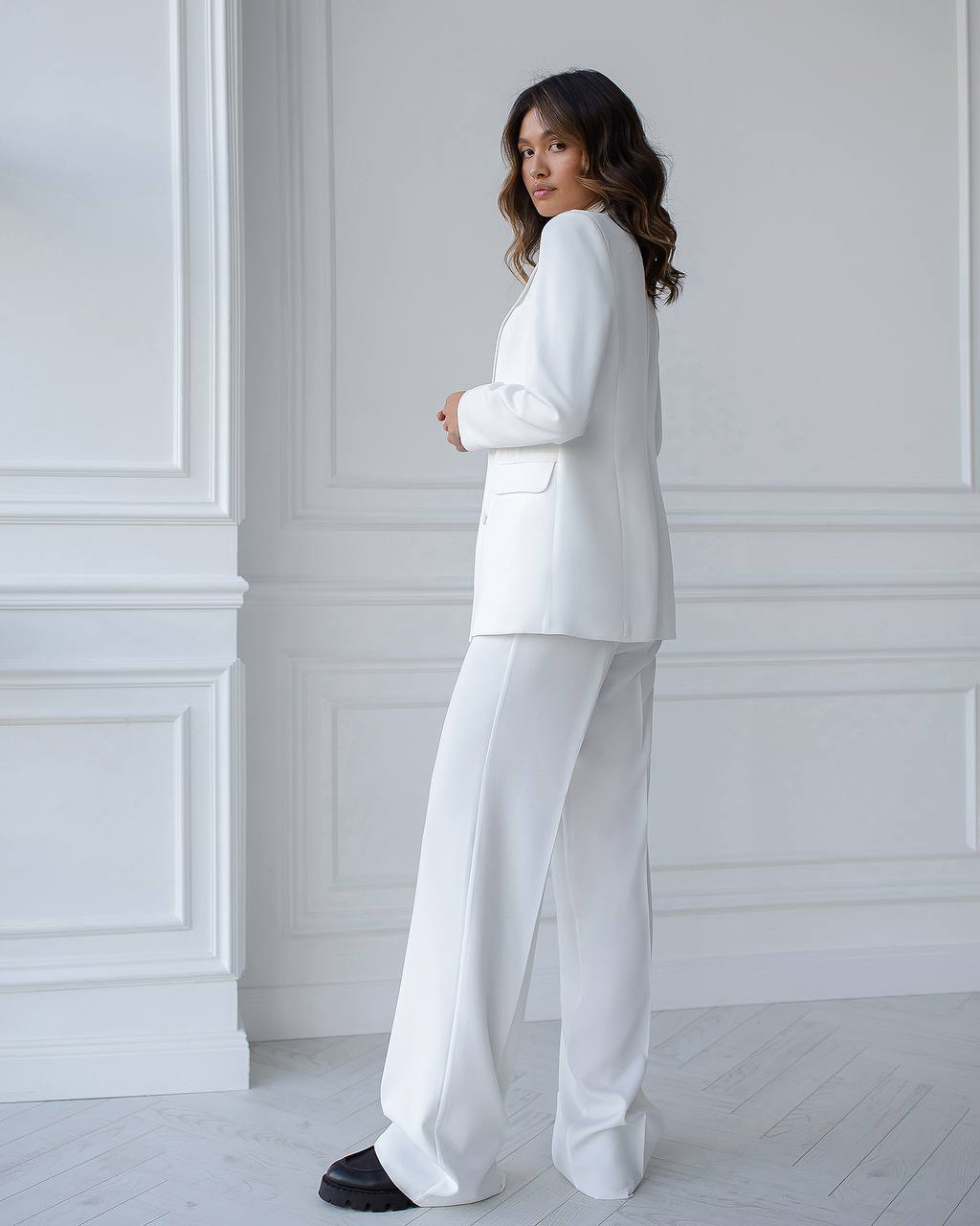 Woman wearing a white suit standing against a white wall