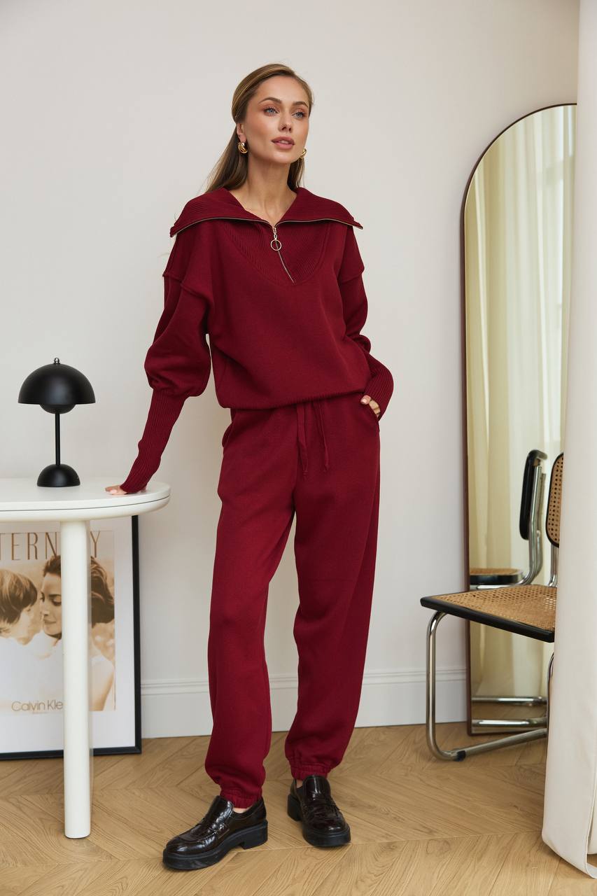 Woman in a red outfit standing in a room with a mirror and table.