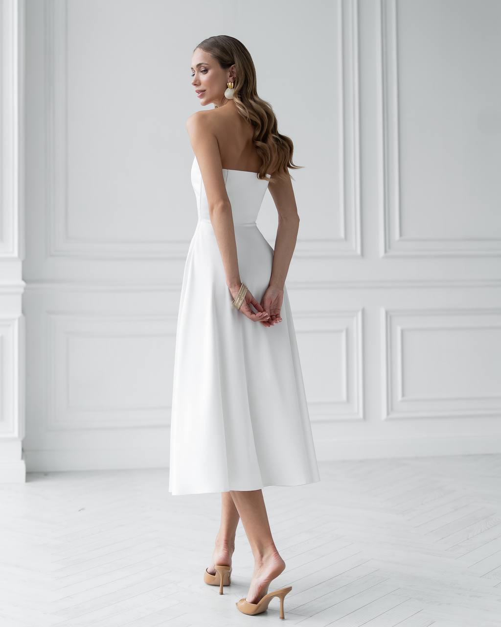 Woman wearing a white strapless dress against a white wall