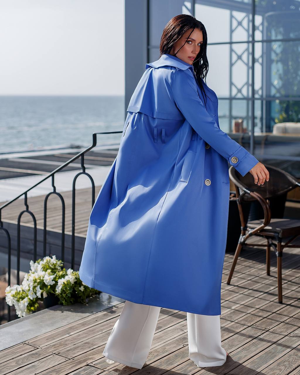 Woman wearing a blue coat standing on a wooden deck by the sea.