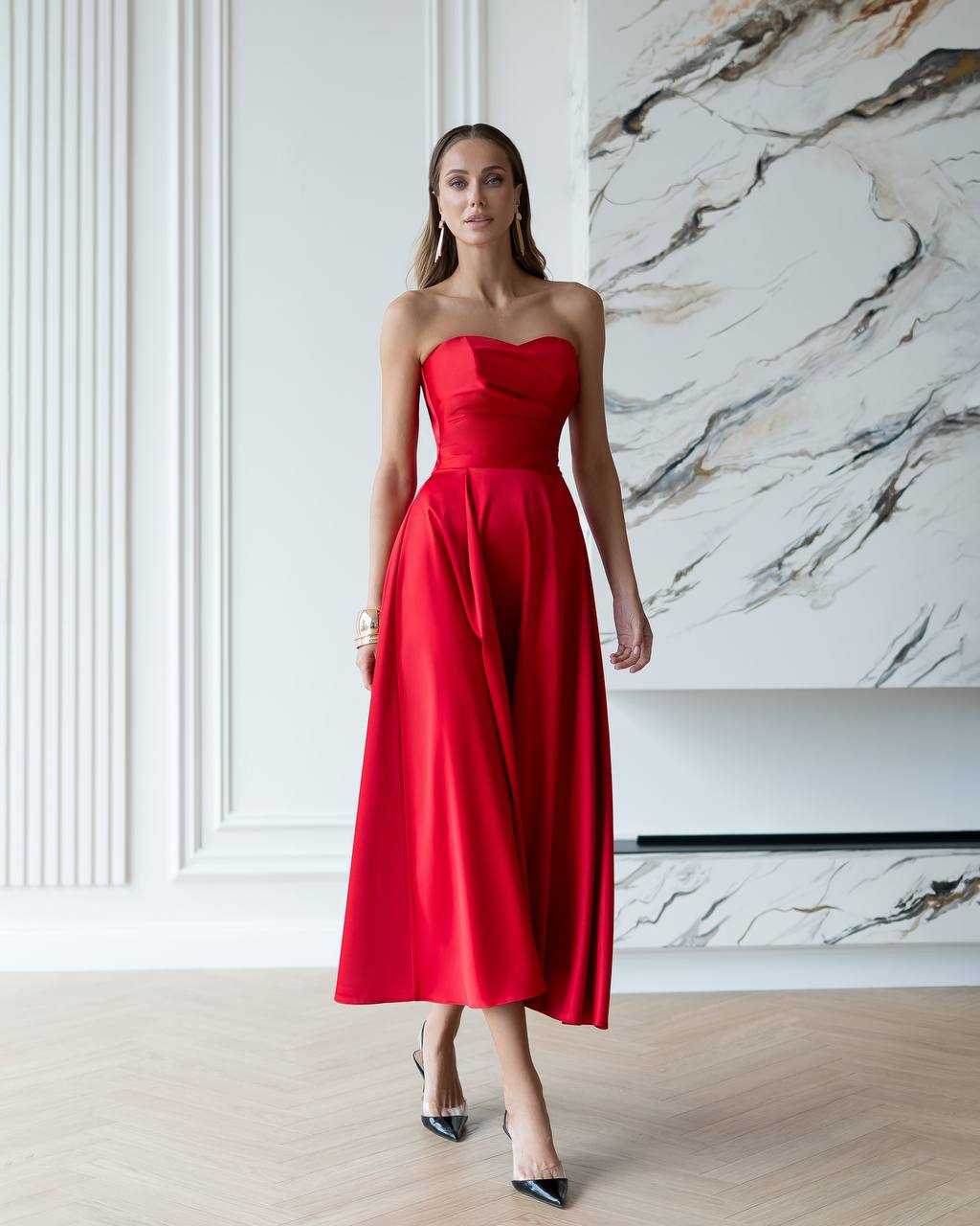 Woman wearing a red strapless dress in a room with marble wall.