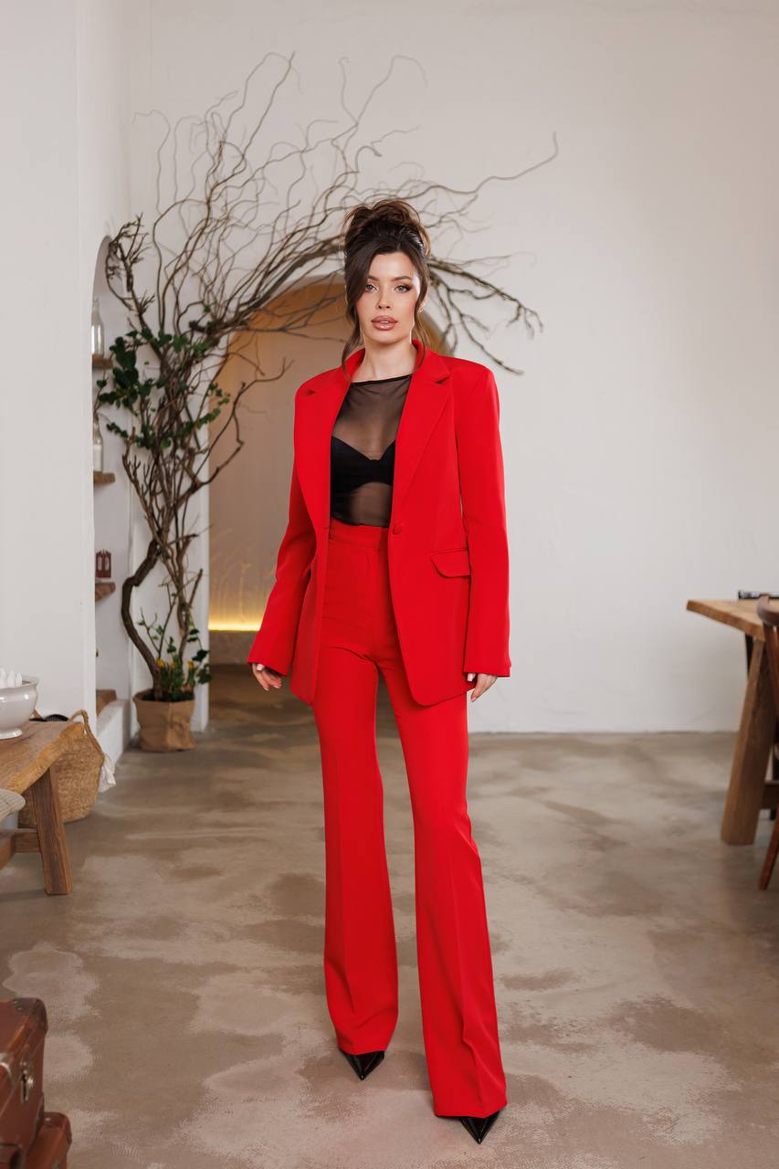 Woman in a red suit standing in an indoor setting with a neutral background
