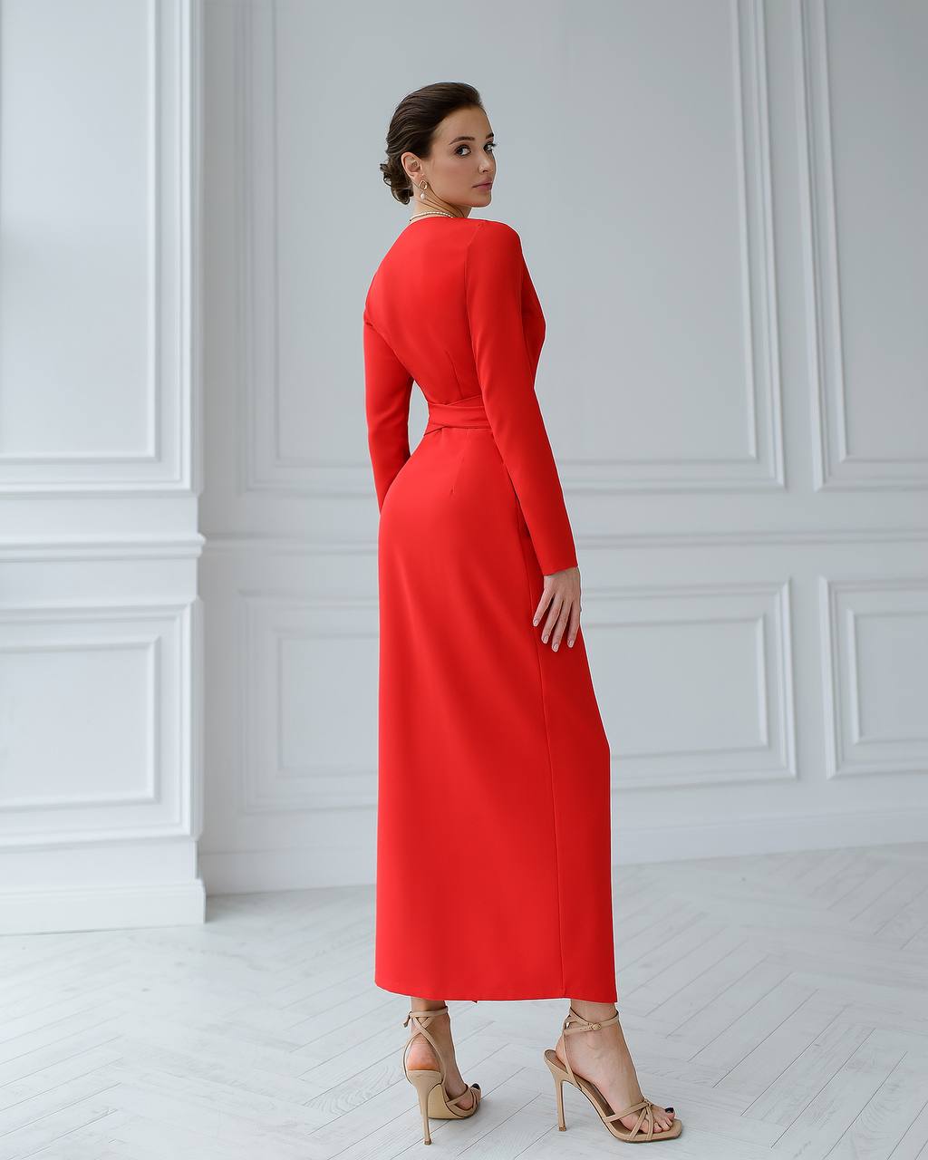 Woman wearing a red dress standing against a white wall.