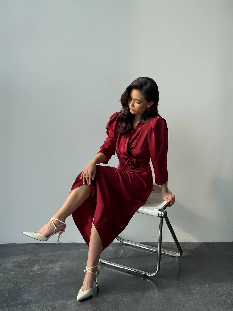 Woman in a red dress sitting on a chair against a gray background
