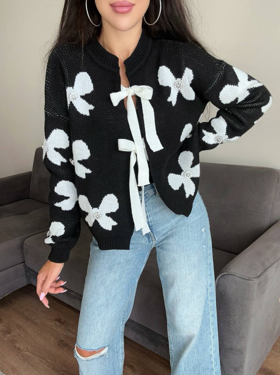 Person wearing a black cardigan with white bow patterns and light blue jeans in a living room setting.