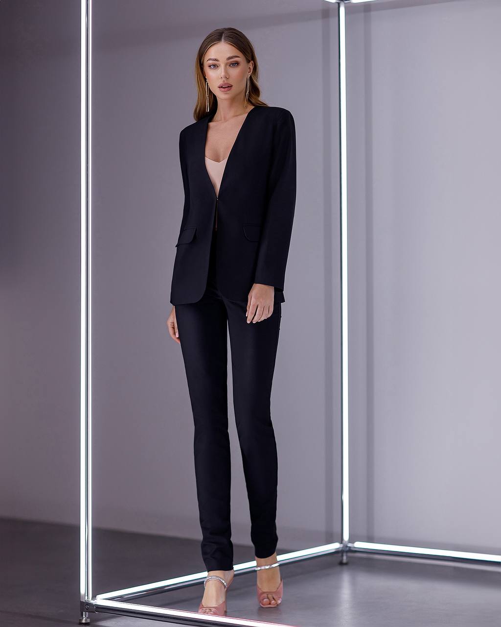 Woman wearing a black suit standing inside a reflective, metallic box.
