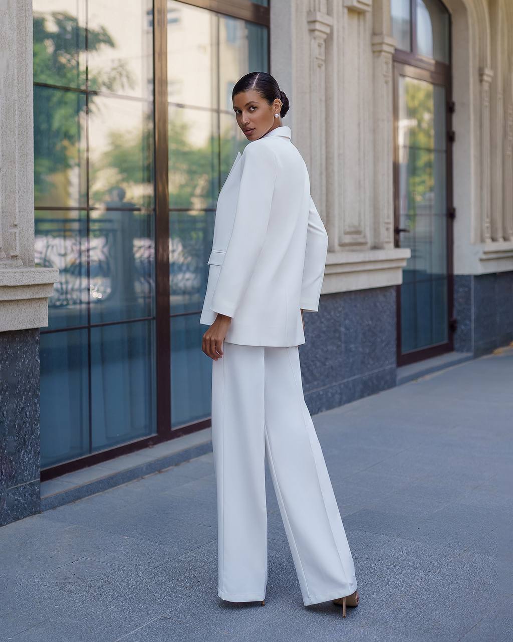 Woman in a white suit standing in front of a building with large windows.