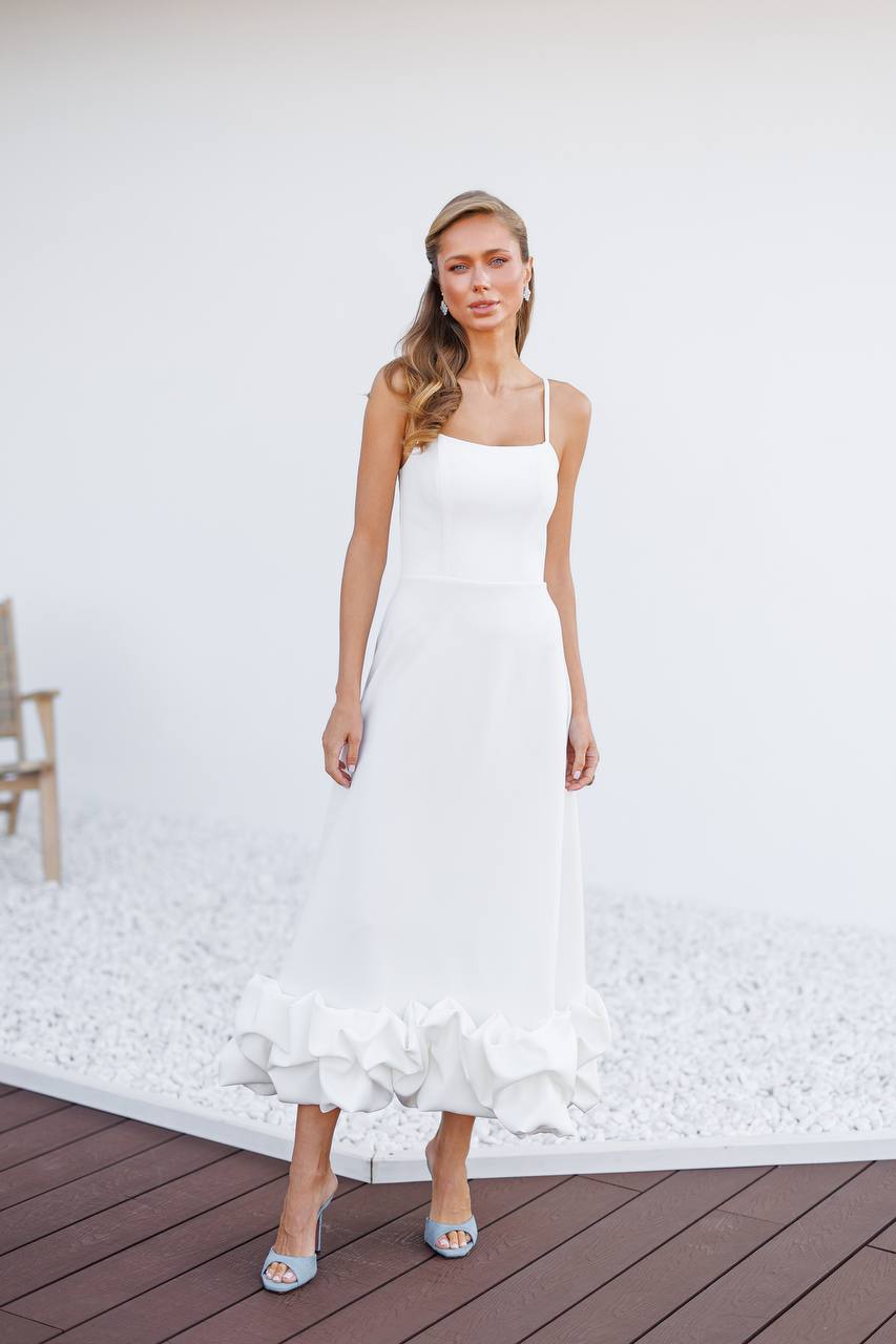Woman wearing a white dress with ruffled details on a wooden deck.